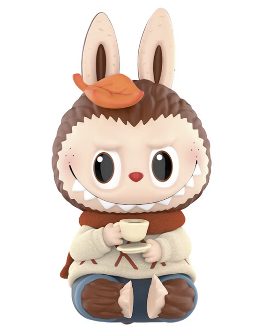 Pop Mart The Monsters ZIMOMO Warm Sweater Figure, featuring ZIMOMO with oversized ears, a cream knitted sweater, brown scarf and blue trousers, sitting and holding a miniature cup of hot chocolate against a white background.