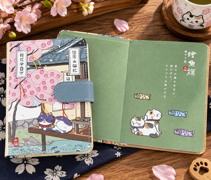 MUROO Shanmao Sakura Cat notebook beside open green illustrated inside cover with cats and colourful fish flags