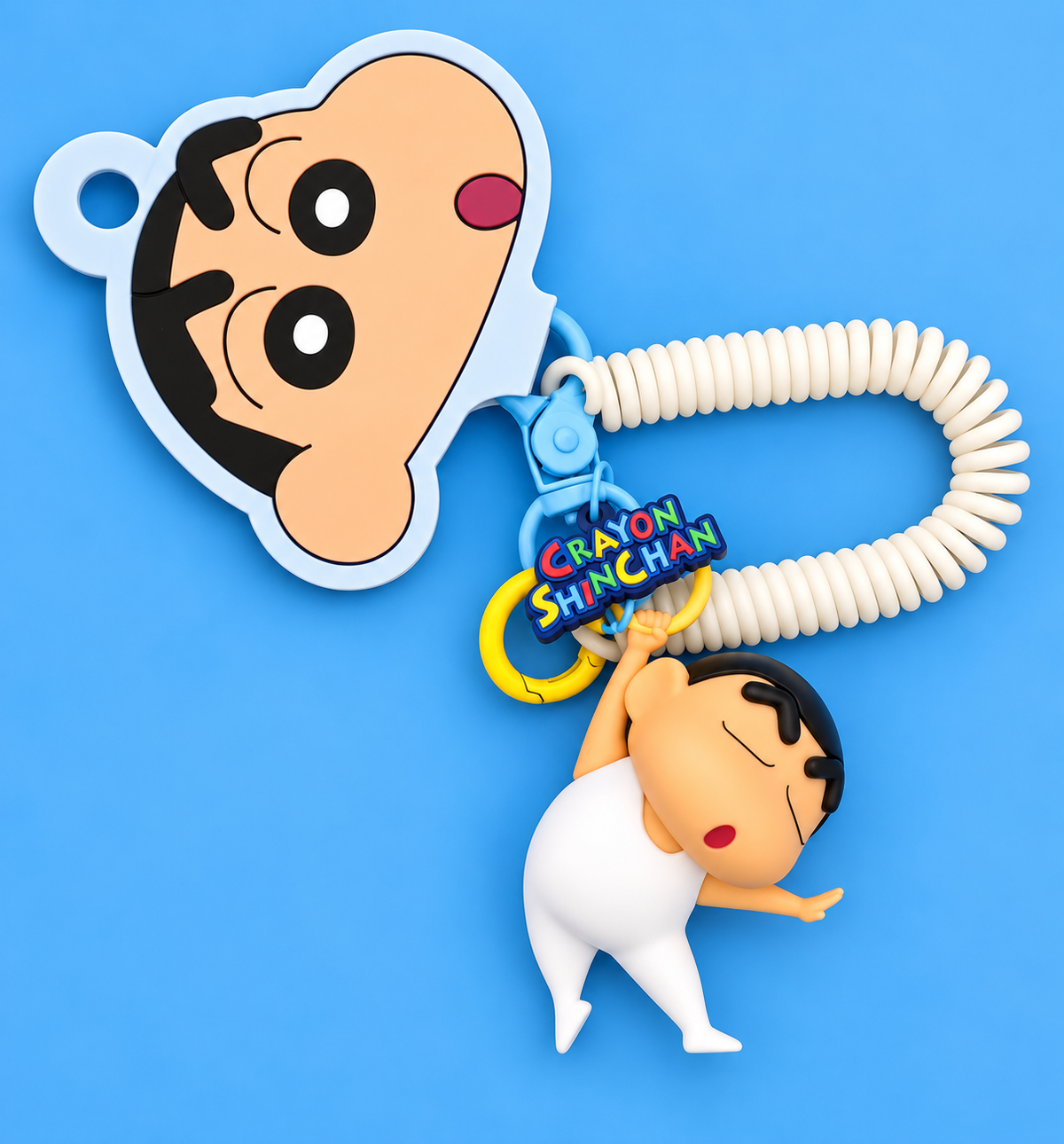 Miniso Crayon Shin-chan keychain featuring a 3D Shin-chan figure, cream spiral wrist strap, blue clip, colourful logo charm and original character cardboard tag against a blue background.