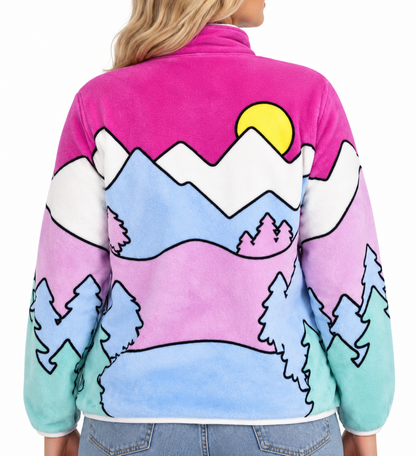 Blonde woman wearing Hello Kitty fleece jacket, showing the pastel mountain and forest landscape across the back and sleeves.