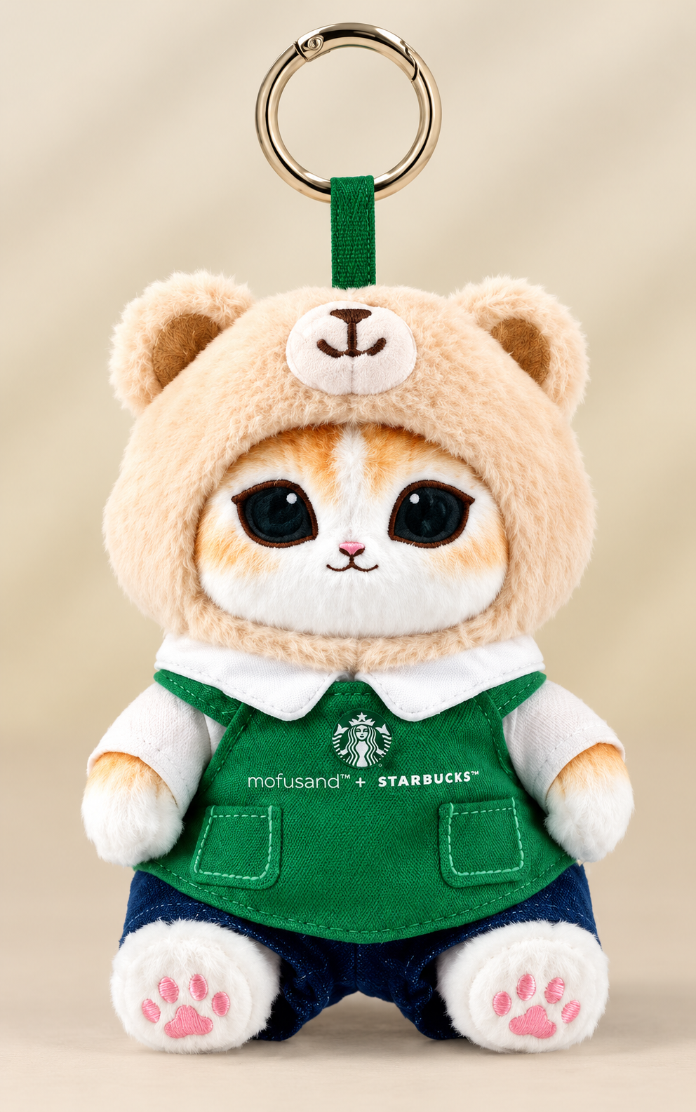 Starbucks × Mofusand Singapore-exclusive 2026 ginger cat Bearista plush keychain wearing a beige teddy bear hood, green Starbucks apron and navy shorts.
