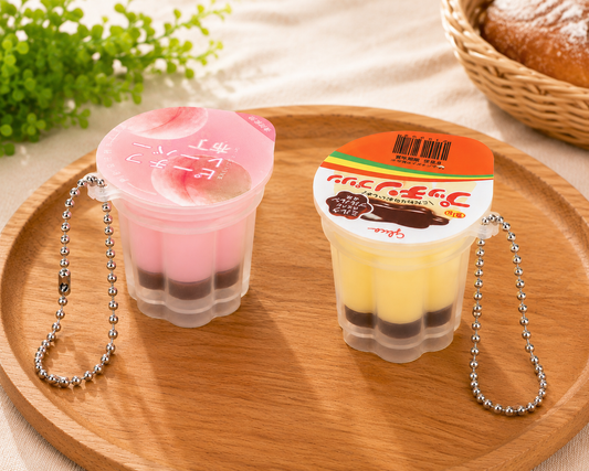 Pink peach and yellow Japanese-style pudding squishy keyrings with silver ball chains displayed on a wooden tray.