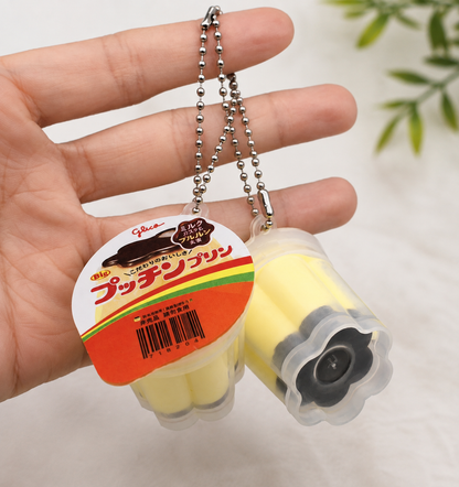 Yellow Japanese-style pudding squishy keyring shown in a hand to demonstrate its size and silver ball chain.