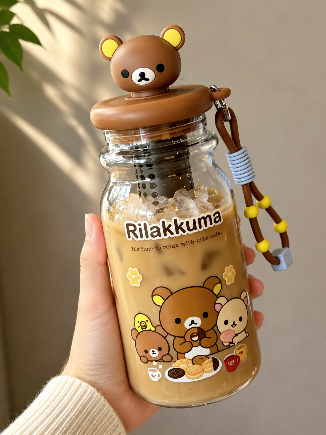 Rilakkuma 3D bear head drinks bottle held in hand and filled with iced coffee, showing character artwork, internal filter and brown carry strap