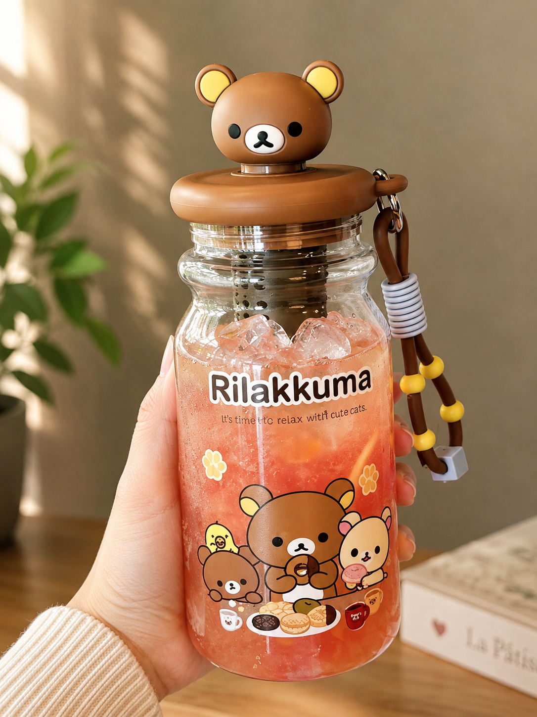 Rilakkuma clear character bottle held in hand and filled with pink iced fruit drink, featuring 3D bear head lid, internal infuser and decorative strap