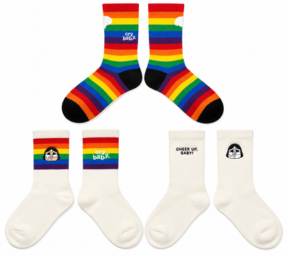 Three pairs of Pop Mart CRYBABY Cheer Up, Baby! socks featuring colourful rainbow stripes, embroidered CRYBABY characters and Cheer Up Baby lettering.