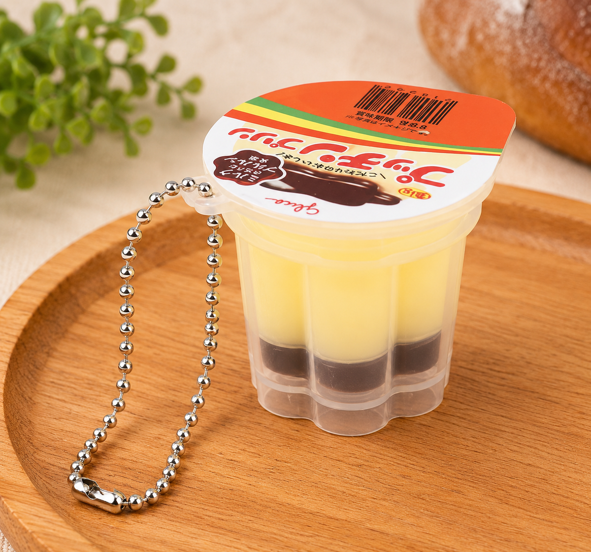 Yellow custard Japanese-style pudding squishy keyring with brown caramel layer and silver ball chain on a wooden tray.